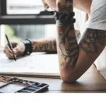 ragazza con braccia tatuate disegna un tatuaggio