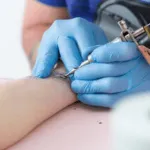 mani con guanti celesti che fanno un tatuaggio sul polso si una persona