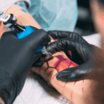 mani con guanti neri che tatuano spidreman su un braccio