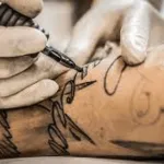 mani con guanti monouso bianco che tatua una scritta su un braccio